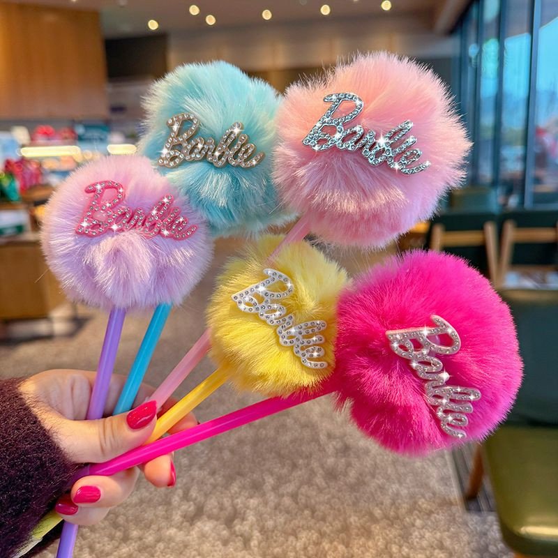 Stylos à pompon en peluche Barbie se distinguent par leurs boules duveteuses aux couleurs pastel et éclatantes, surmontées de l'inscription « Barbie » en strass scintillants.